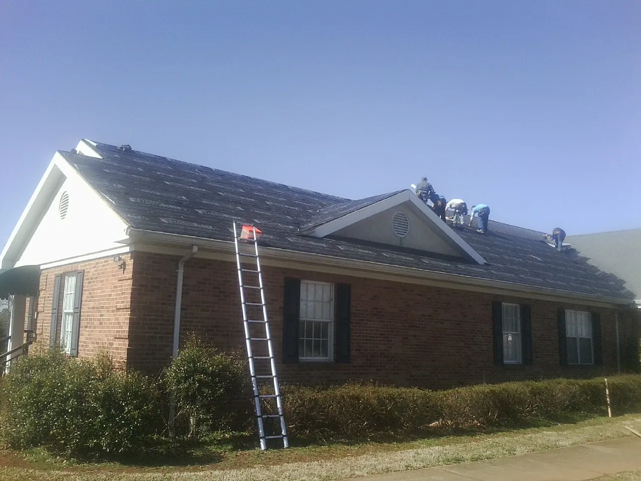 Crew tearing shingles off a brick ranch roof with a ladder set — Emergency Roof Repair work by our crew in Cape Girardeau