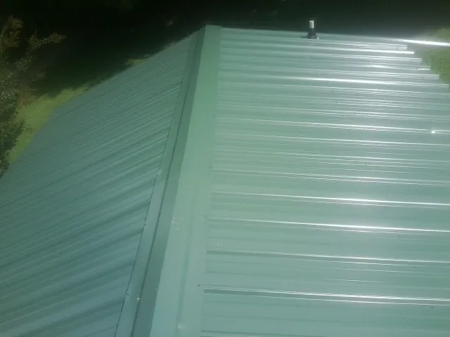 New green metal panels meeting at the ridge of a roof — Flat Roof Repair work by our crew in Cape Girardeau