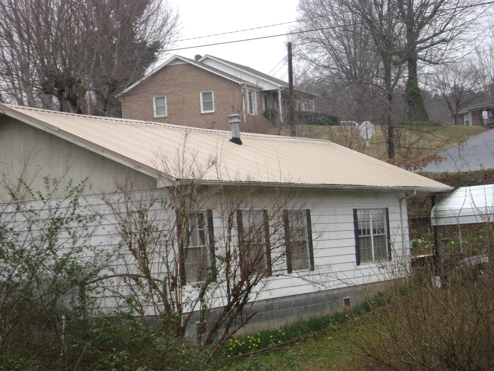 Tan metal roof on a white sided house set into a hillside — Commercial Roofing by Roofing Brothers in Cape Girardeau
